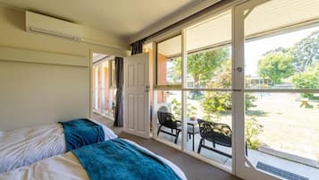 Una habitación con dos camas y un ventanal corredero que da a un espacio exterior con una mesa y sillas.