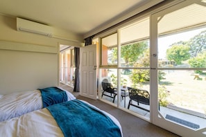 A room with two beds, a sliding glass door leading to an outdoor area with a table and chairs.