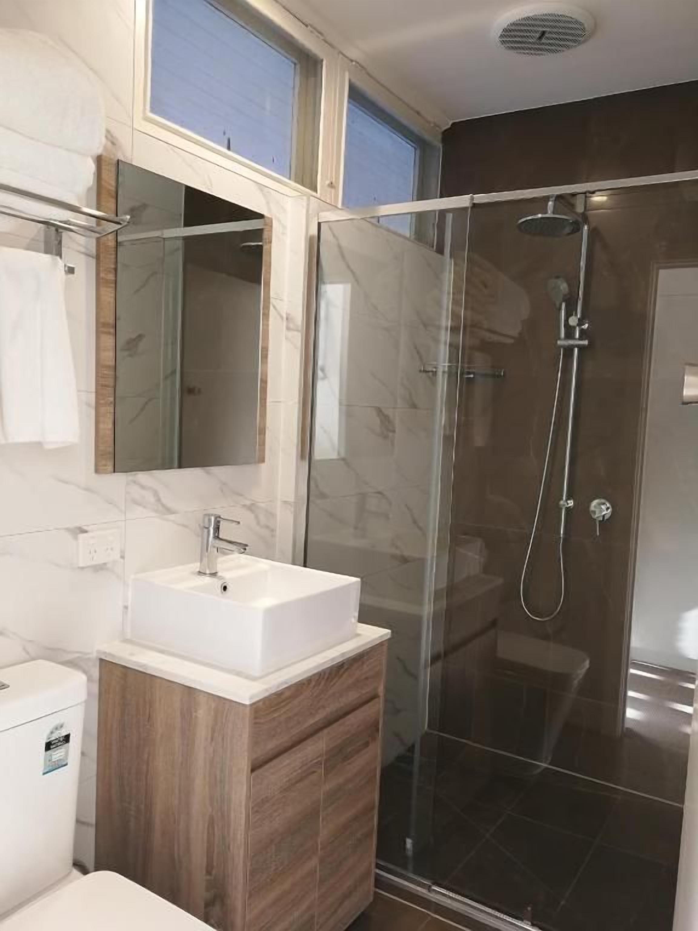 A bathroom with a glass-enclosed shower, a white sink, and a wooden vanity.