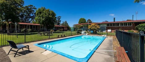 A swimming pool with a basketball court, surrounded by a fence, benches, and trees.