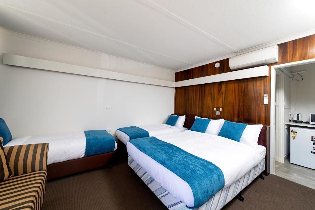 Ein Hotelzimmer mit drei Betten, einer Küchenzeile und einer Wand mit Holzelementen.
