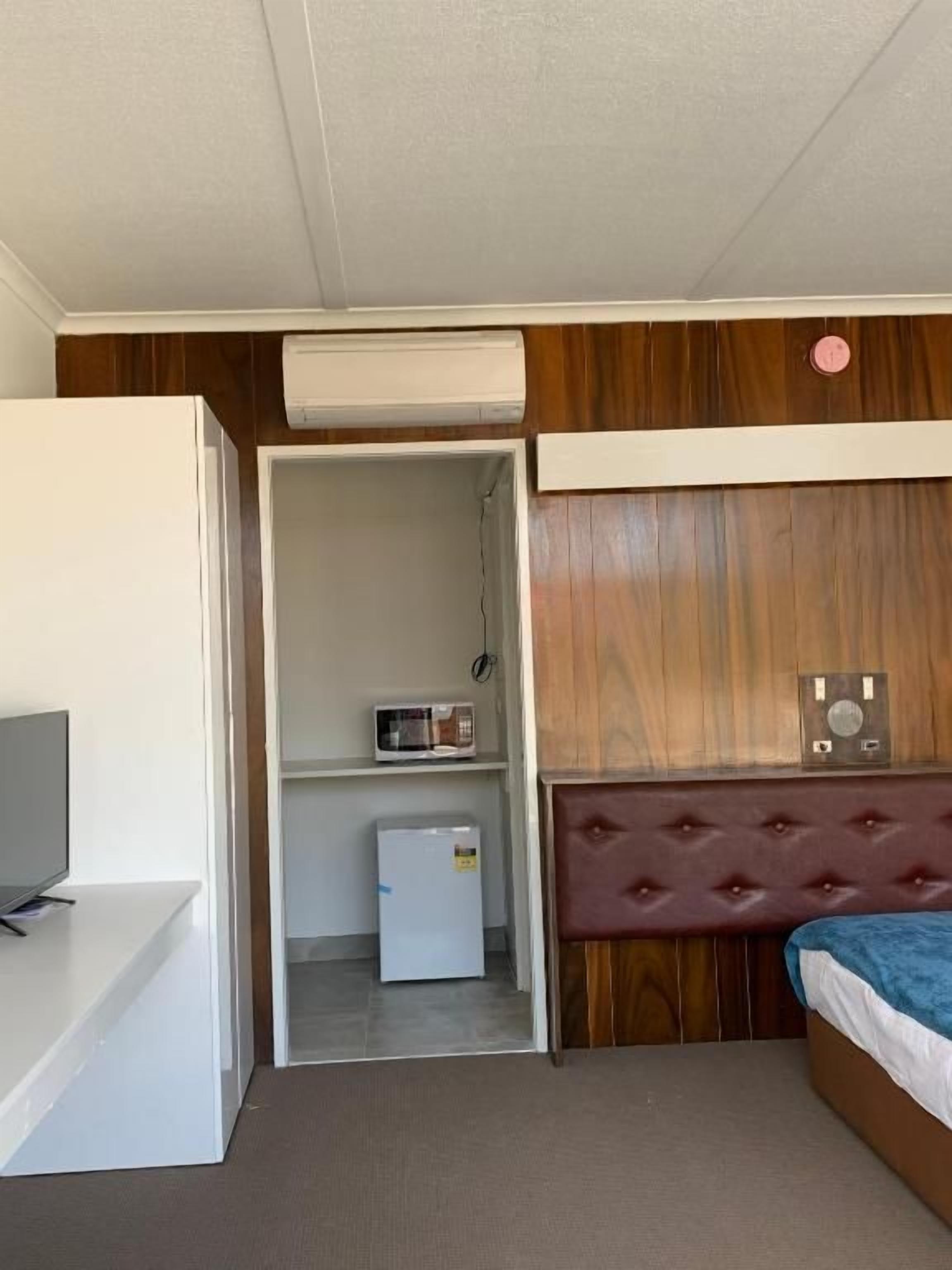 Une chambre de taille modeste comprenant un lit, une petite kitchenette, un téléviseur et une armoire.