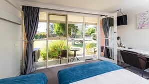 Habitación de hotel con dos camas, un escritorio, una silla, un televisor y una puerta corrediza de vidrio que da a un área exterior.