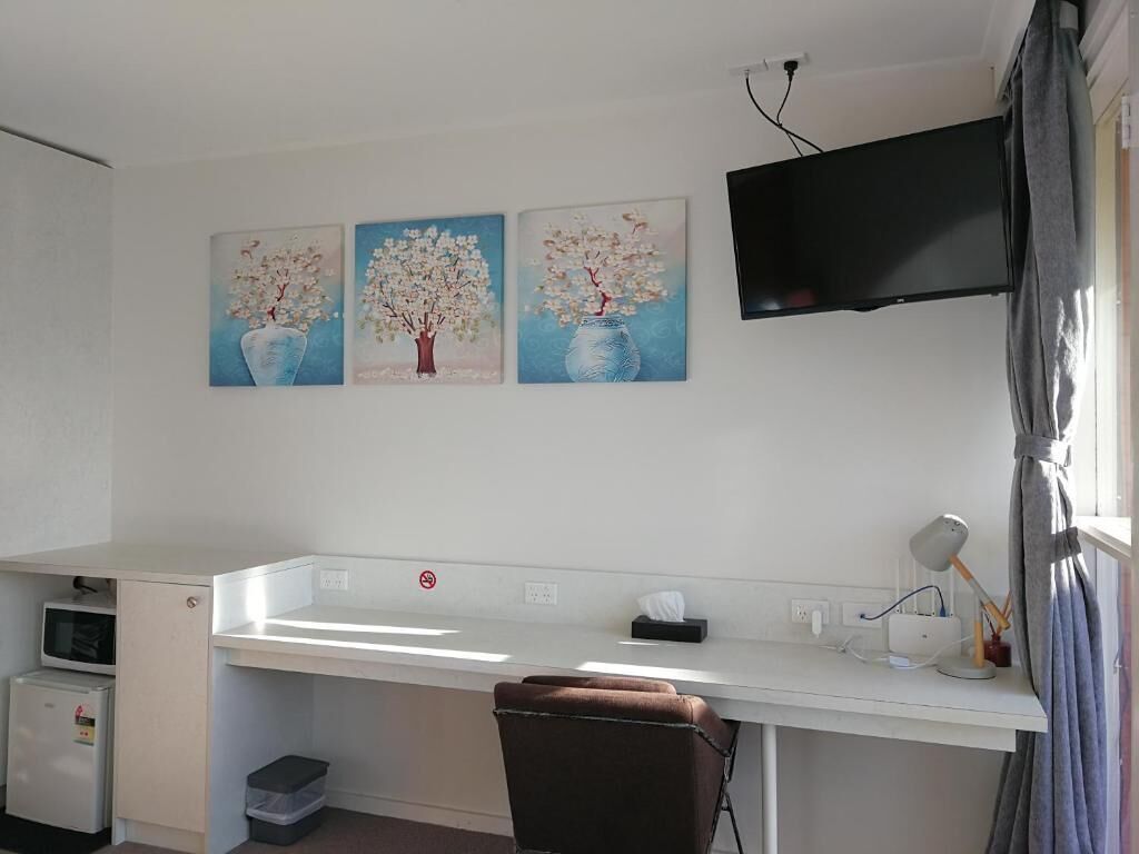 Una habitación con un escritorio, una silla, un televisor de pantalla plana montado en la pared y tres cuadros con árboles en jarrones.