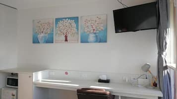 Una habitación con un escritorio, una silla, un televisor de pantalla plana montado en la pared y tres cuadros con árboles en jarrones.
