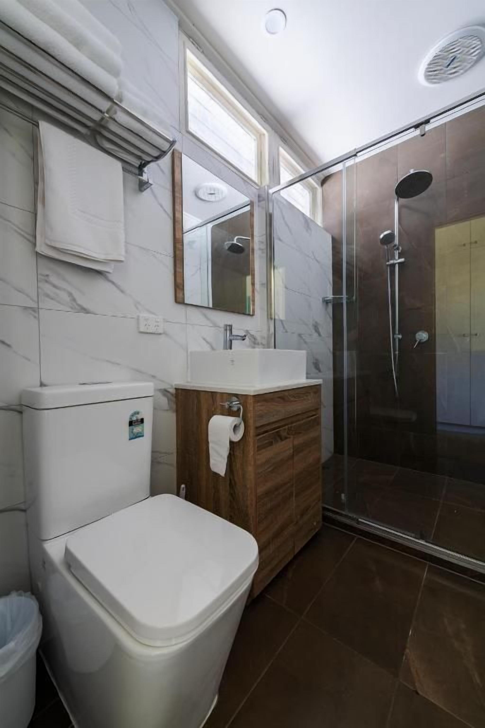 Un baño con inodoro, lavamanos, tocador y zona de ducha con mampara de vidrio.