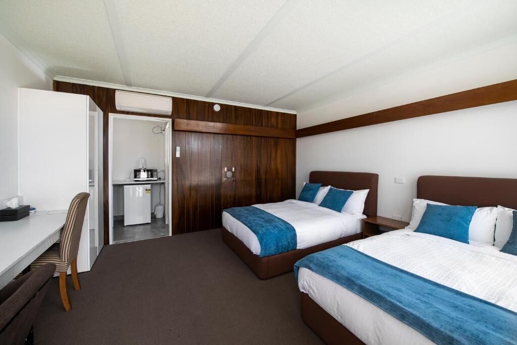 A hotel room with two beds, a desk, and a small kitchenette.