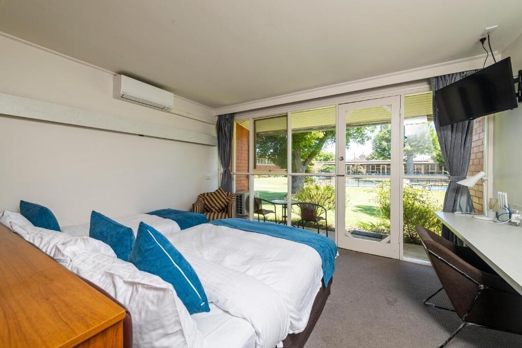 A hotel room with a bed, a desk, a television, and a sliding glass door leading to a balcony.