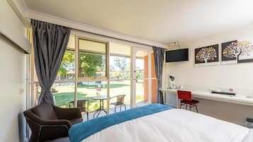 Une chambre d’hôtel avec un lit, un bureau, une chaise et une grande fenêtre avec des rideaux.