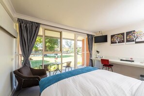 Una habitación de hotel con una cama, un escritorio, una silla y un ventanal con cortinas.