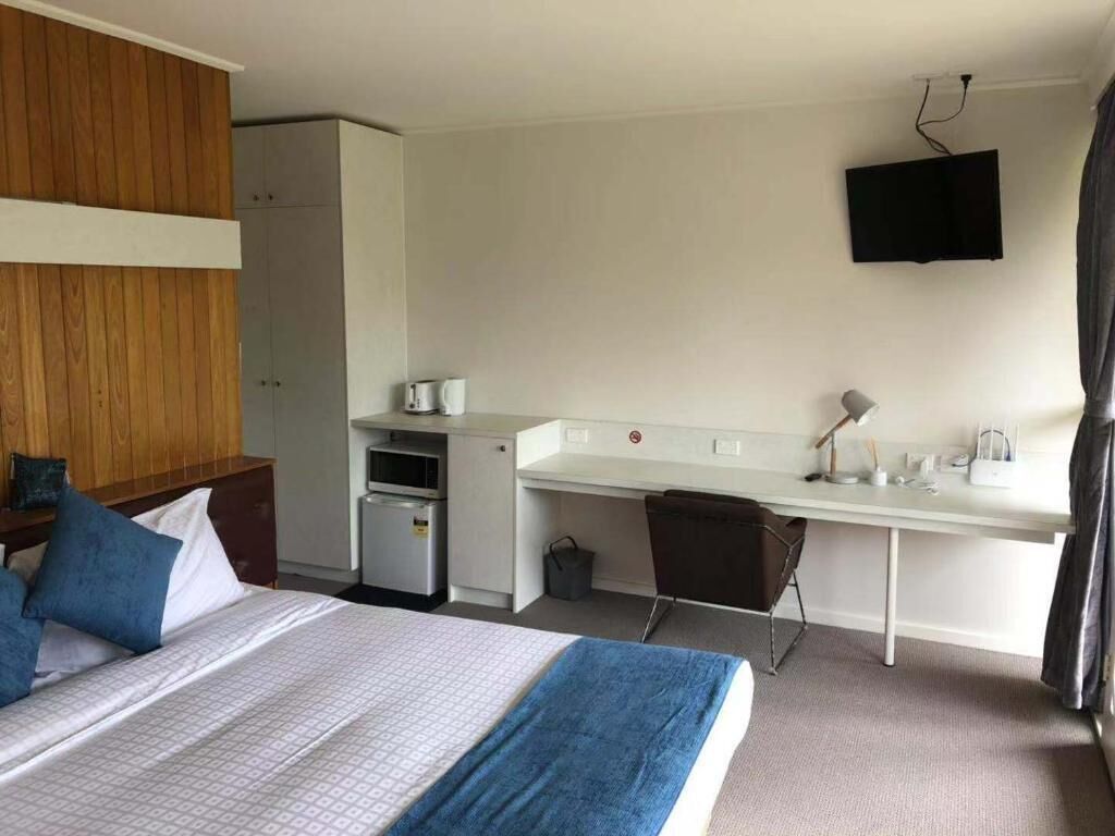 Una habitación de hotel con cama, escritorio, televisor y kitchenette.
