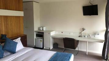 Una habitación de hotel con cama, escritorio, televisor y kitchenette.