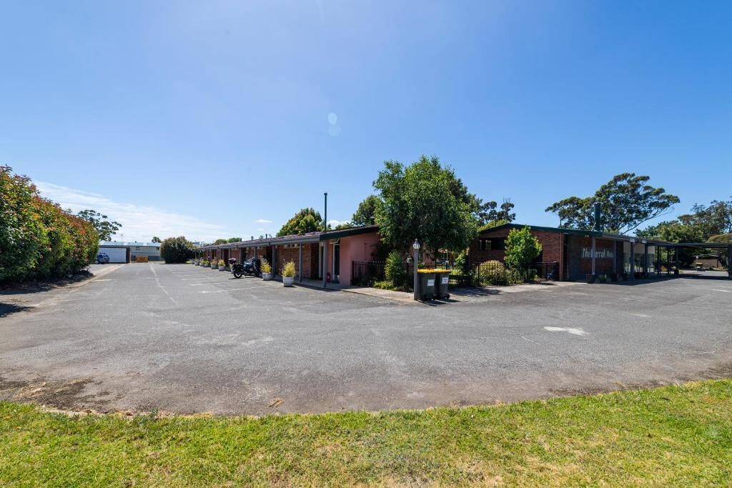 A parking lot with a row of single-story buildings, likely a motel or hotel, with a clear sky above.