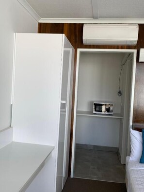 Habitación pequeña con un armario blanco, un microondas en un estante y una cama con una almohada.