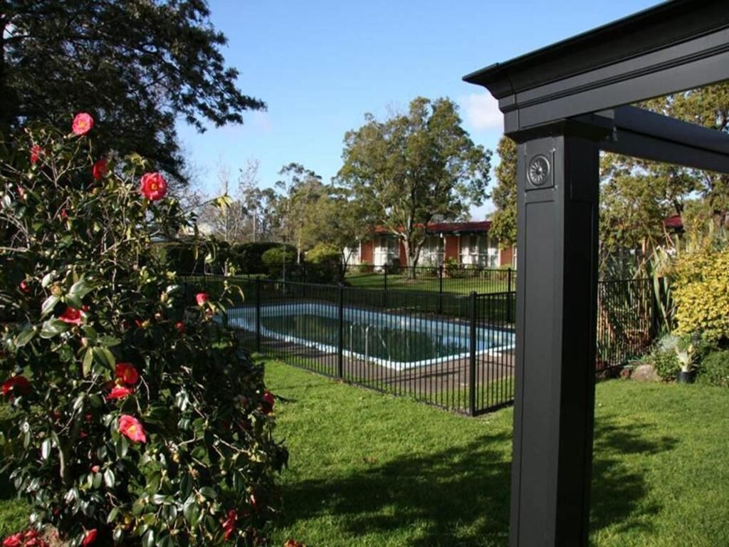 Una piscina rodeada por una valla negra, con un jardín y árboles al fondo.