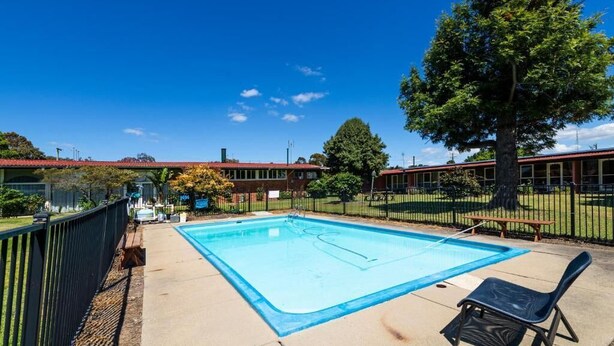 Una piscina con línea de agua azul cristalina, rodeada por un solárium de hormigón y una valla de metal negro.