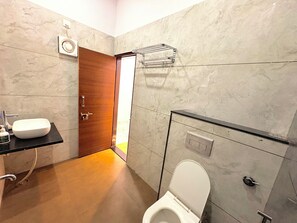 Un baño con inodoro blanco, puerta de madera, pared de mármol y encimera negra con lavamanos.