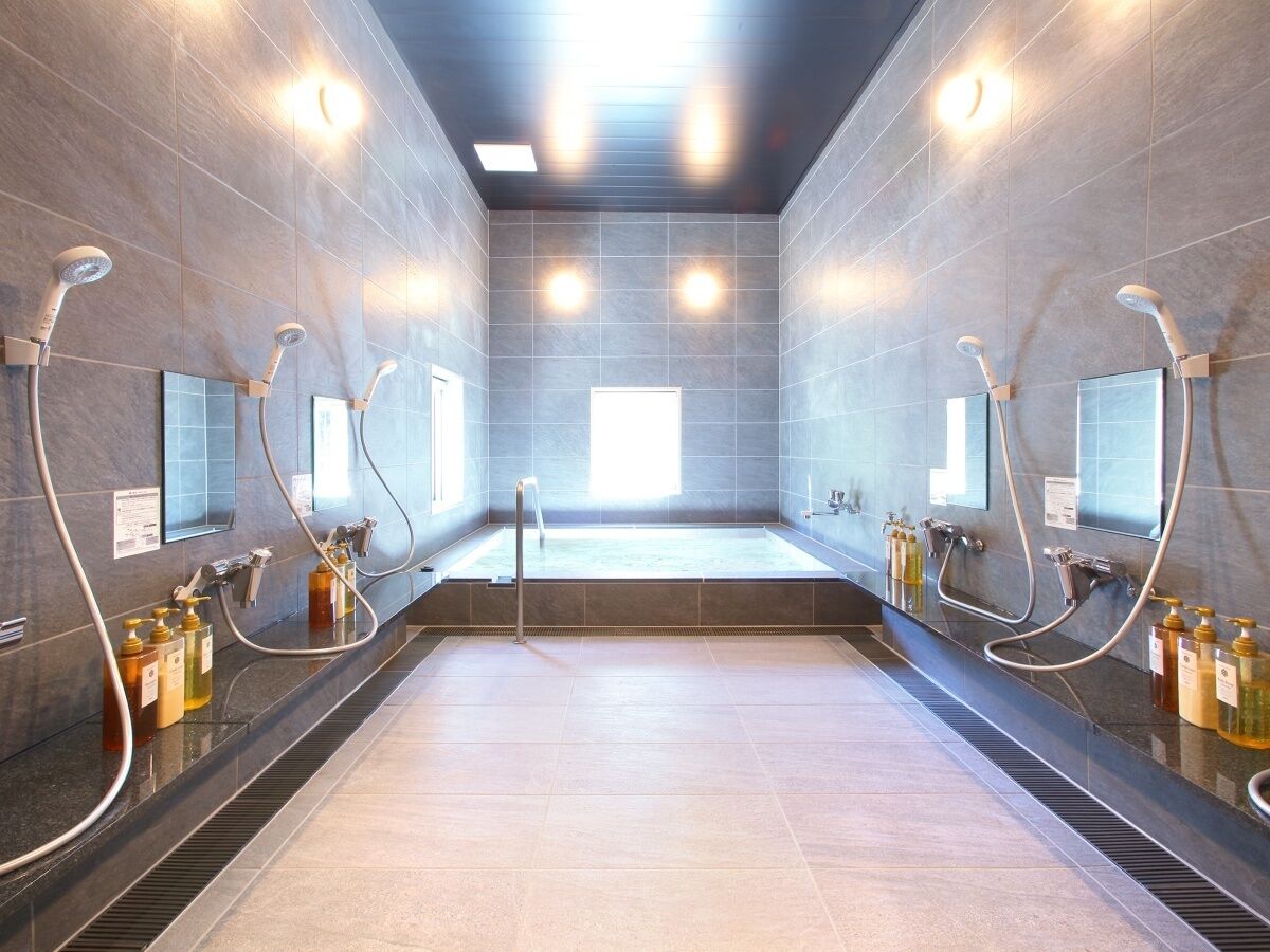 A modern bathroom with multiple showerheads, a large bathtub, and hand sanitizer dispensers.