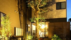 A building with a tree in the foreground, a wooden fence, and air conditioning units on the side. - Gourmet Ryokan Mikawaya (Okawa)