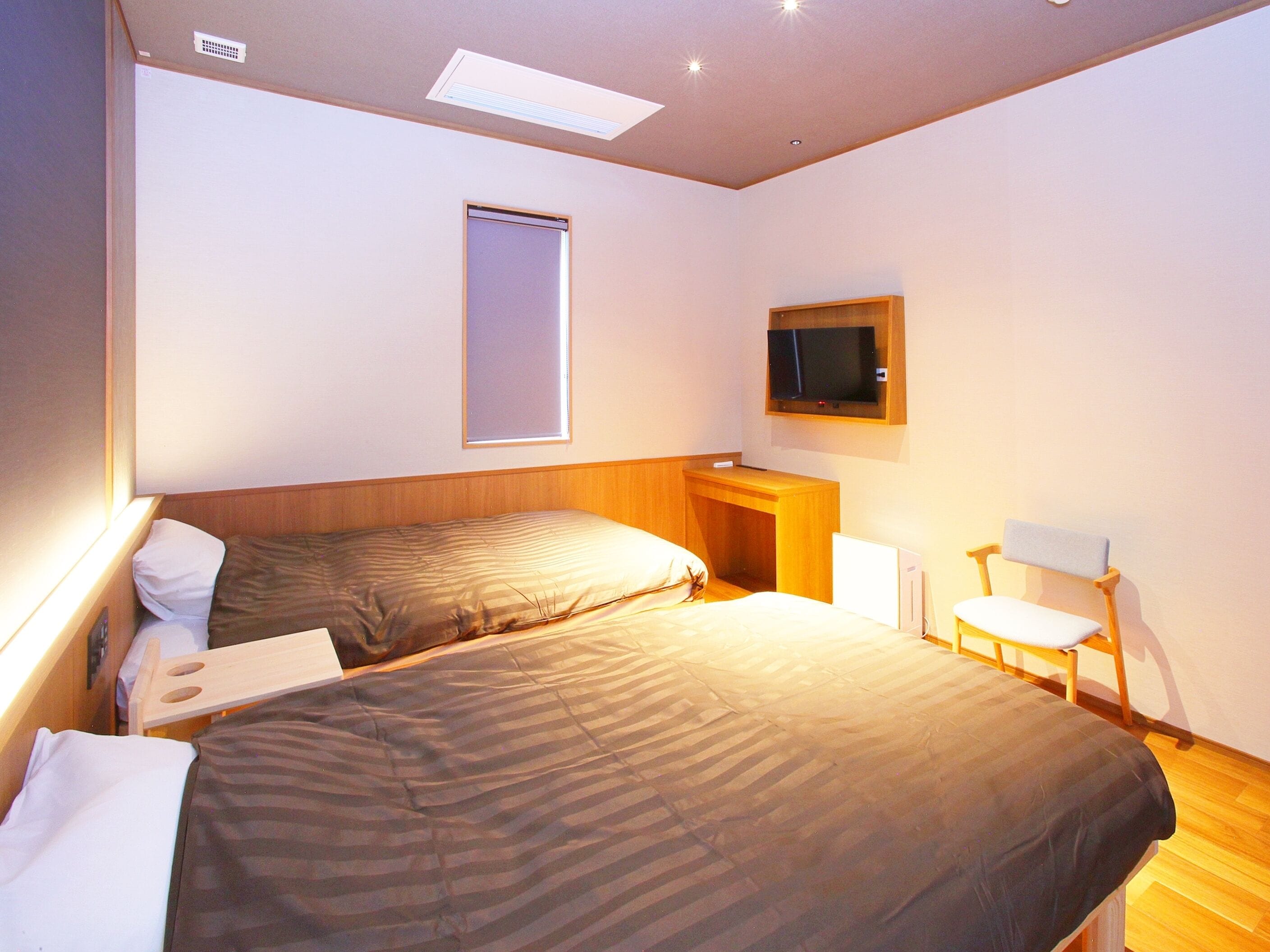 A hotel room with two beds, a television, a desk, and a chair.