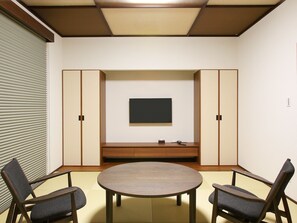 A room with a round table, two chairs, a television on the wall, and wooden cabinets.