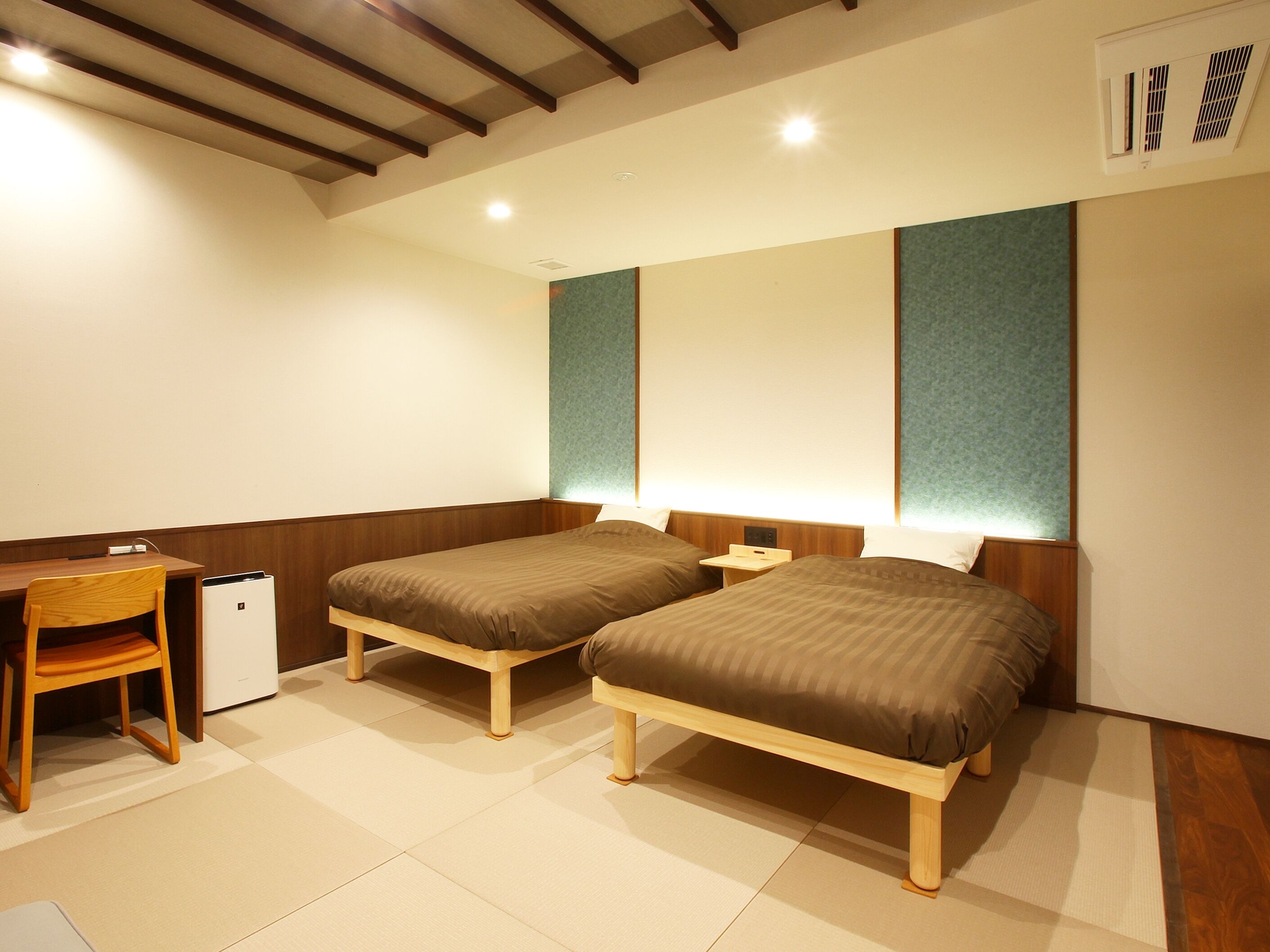 A hotel room with two beds, a desk, a chair, and a small bedside table.