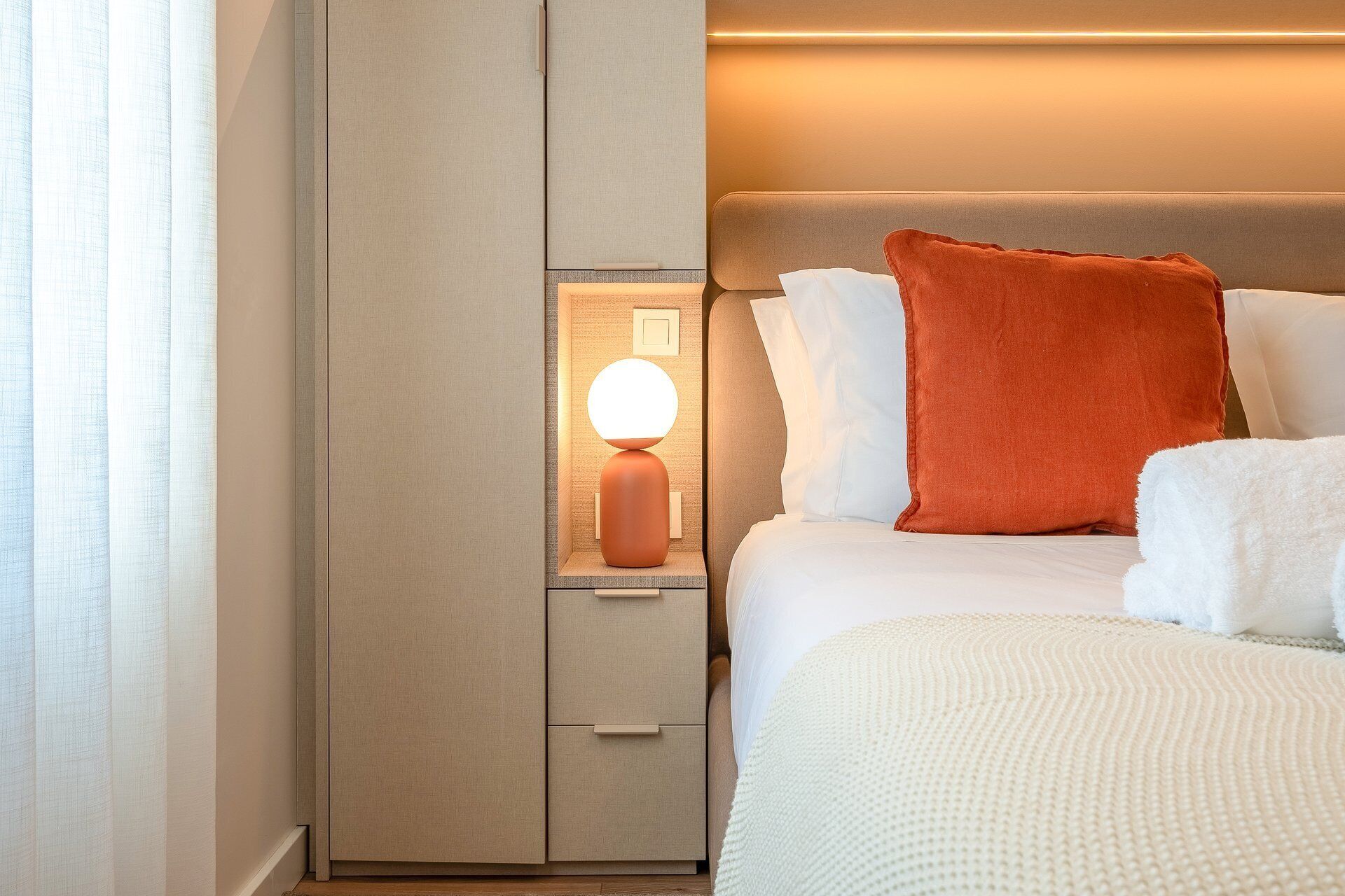 Quarto de hotel com cama, mesa de cabeceira com abajur e guarda-roupa.