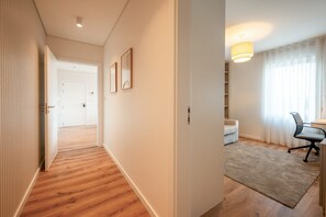 Ein Flur mit Holzboden, der zu einem Raum mit Schreibtisch, Stuhl, einer Couch und einer Lampe führt.