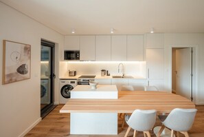A modern kitchen with white cabinetry, a built-in microwave, and a sink. There is a wooden dining table with two chairs. - GuestReady - Maleo Living Apartments - 5C2 (Lisbon)