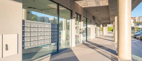 A modern building with large glass windows, a metal fence with mailboxes, and a tiled walkway.
