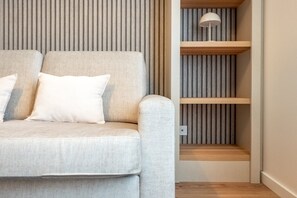 Un canapé avec un coussin, un mur orné de lignes verticales et une étagère sur laquelle se trouve une lampe.
