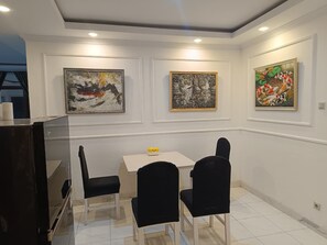 A dining area with a table and chairs, three framed artworks on the wall, and a television on the left. - Spacious 3-bedroom apartment with AC in serene Jogja (Jogja)