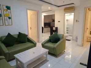 A living room with green sofas and a white coffee table, a kitchen in the background, and a bathroom visible through an open door. - Spacious 3-bedroom apartment with AC in serene Jogja (Jogja)