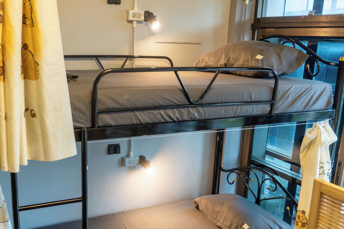 A bunk bed with a window view, a bedside table, and a curtain with a bear pattern.