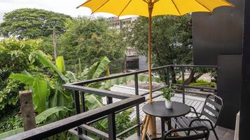 Ein Balkon mit Tisch und Stühlen, einem gelben Sonnenschirm und üppiger Bepflanzung im Hintergrund.