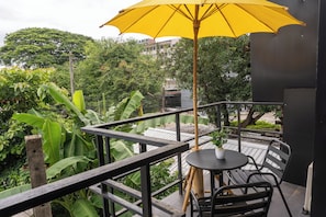 A balcony with a table and chairs, a yellow umbrella, and lush greenery in the background. - Nature's Heaven Hostel (Chiang Mai)