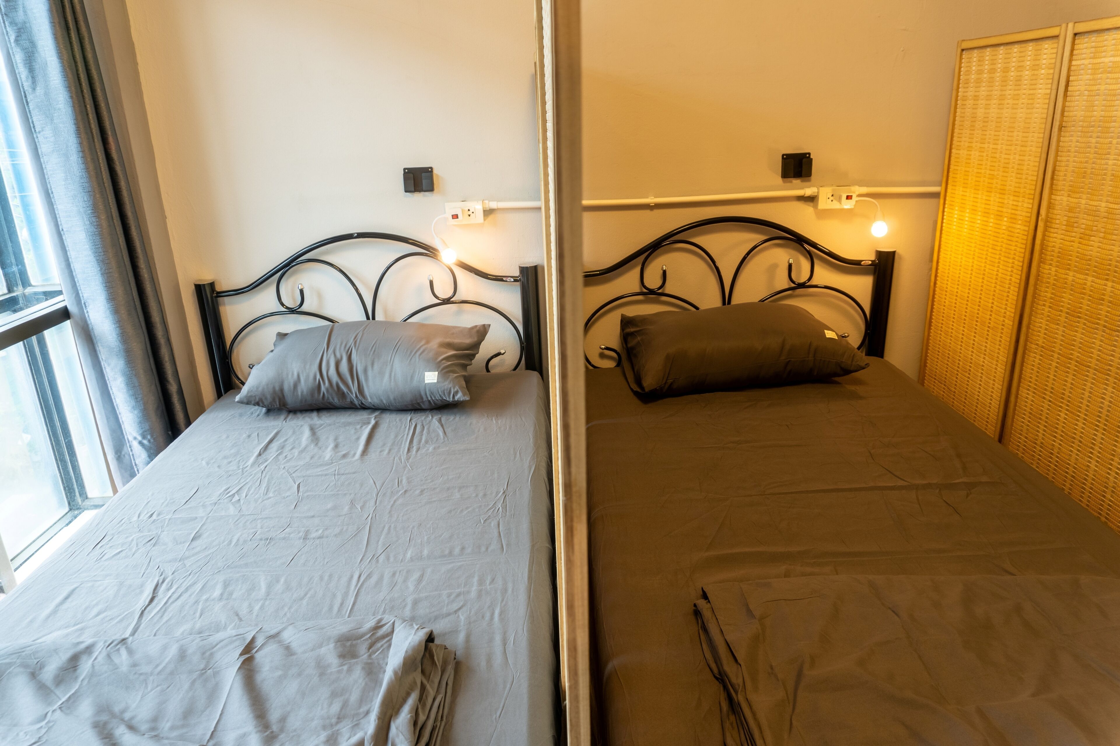 Two single beds with metal frames, a window with curtains, and a wall-mounted light fixture.