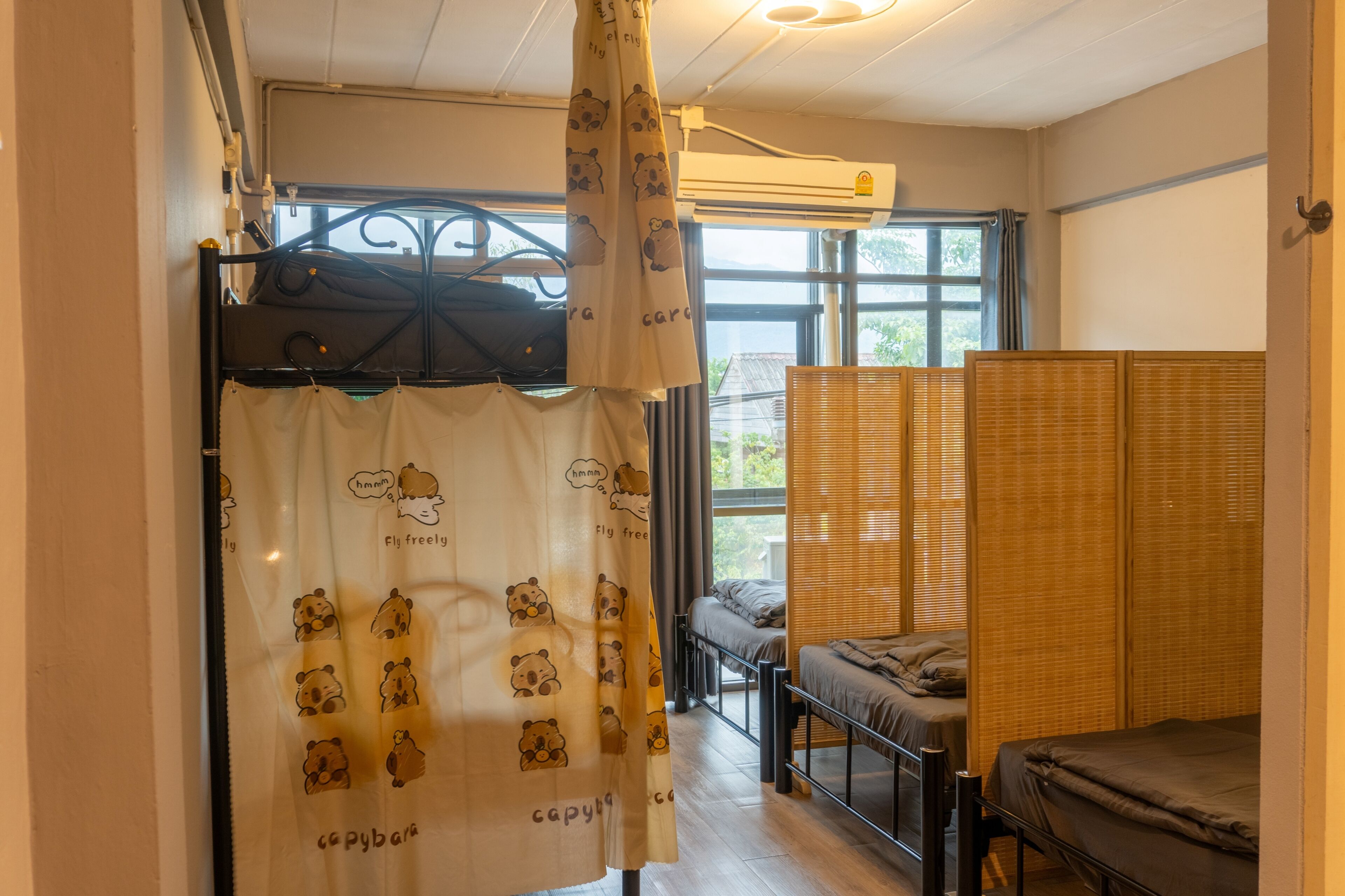Une chambre avec un lit superposé, une fenêtre avec des stores, un rideau orné de motifs d’ours et un ventilateur de plafond.
