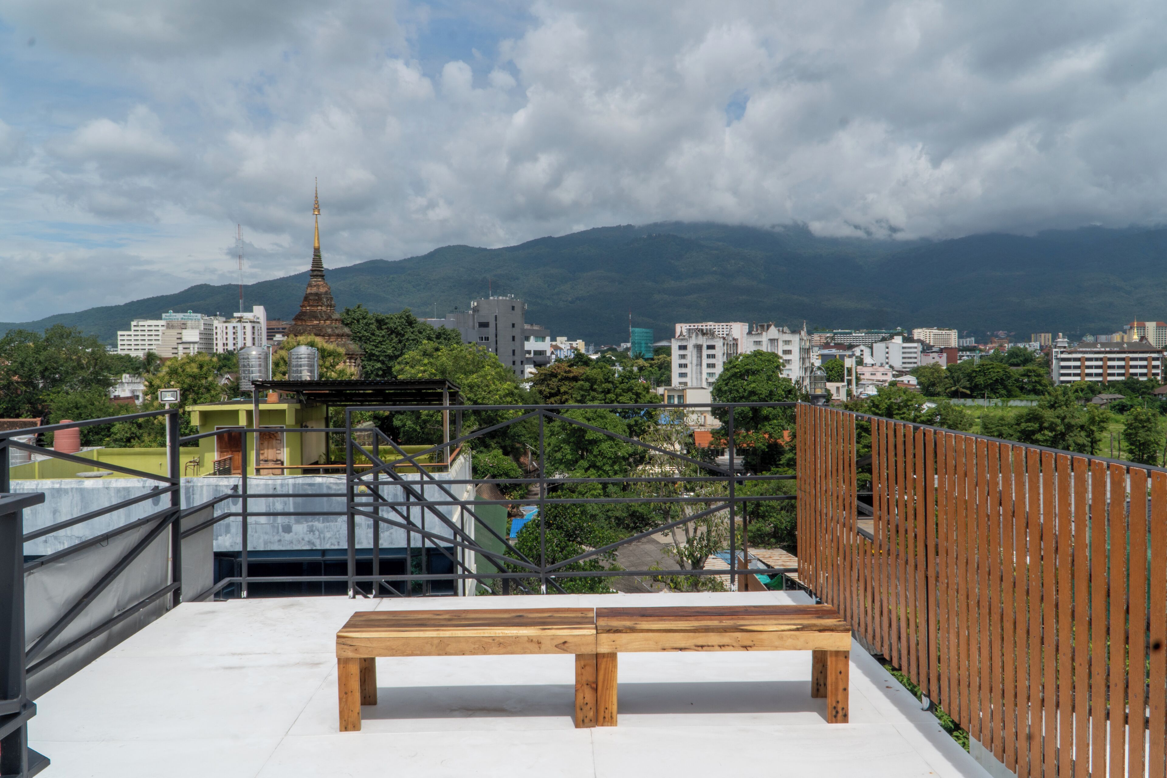 Une terrasse sur le toit avec un banc en bois, une vue sur le paysage urbain et une chaîne de montagnes en arrière-plan.
