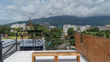Une terrasse sur le toit avec un banc en bois, une vue sur le paysage urbain et une chaîne de montagnes en arrière-plan.