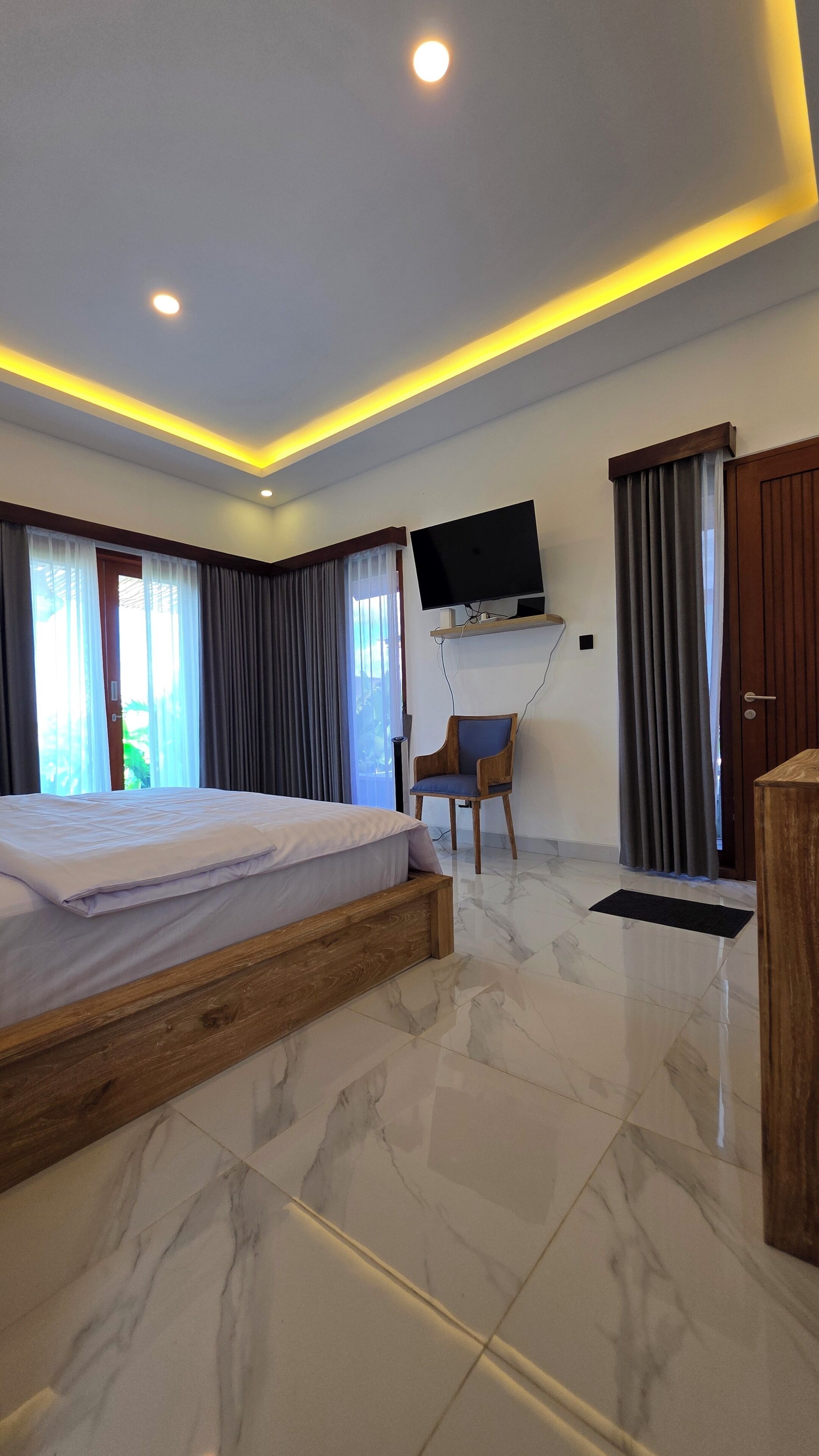 Habitación de hotel con cama, televisor montado en la pared, una silla y una puerta.