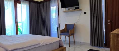 A hotel room with a bed, a television mounted on the wall, a chair, and a door.