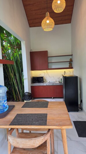 A compact kitchen with a wooden table, two hanging light fixtures, and a water dispenser.