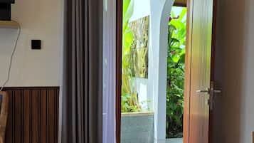 Habitación de hotel con puerta de madera, televisor y vista a un jardín desde una puerta abierta.