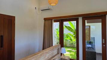 A hotel room with a wooden bed, a bedside lamp, a window with curtains, and an air conditioning unit.
