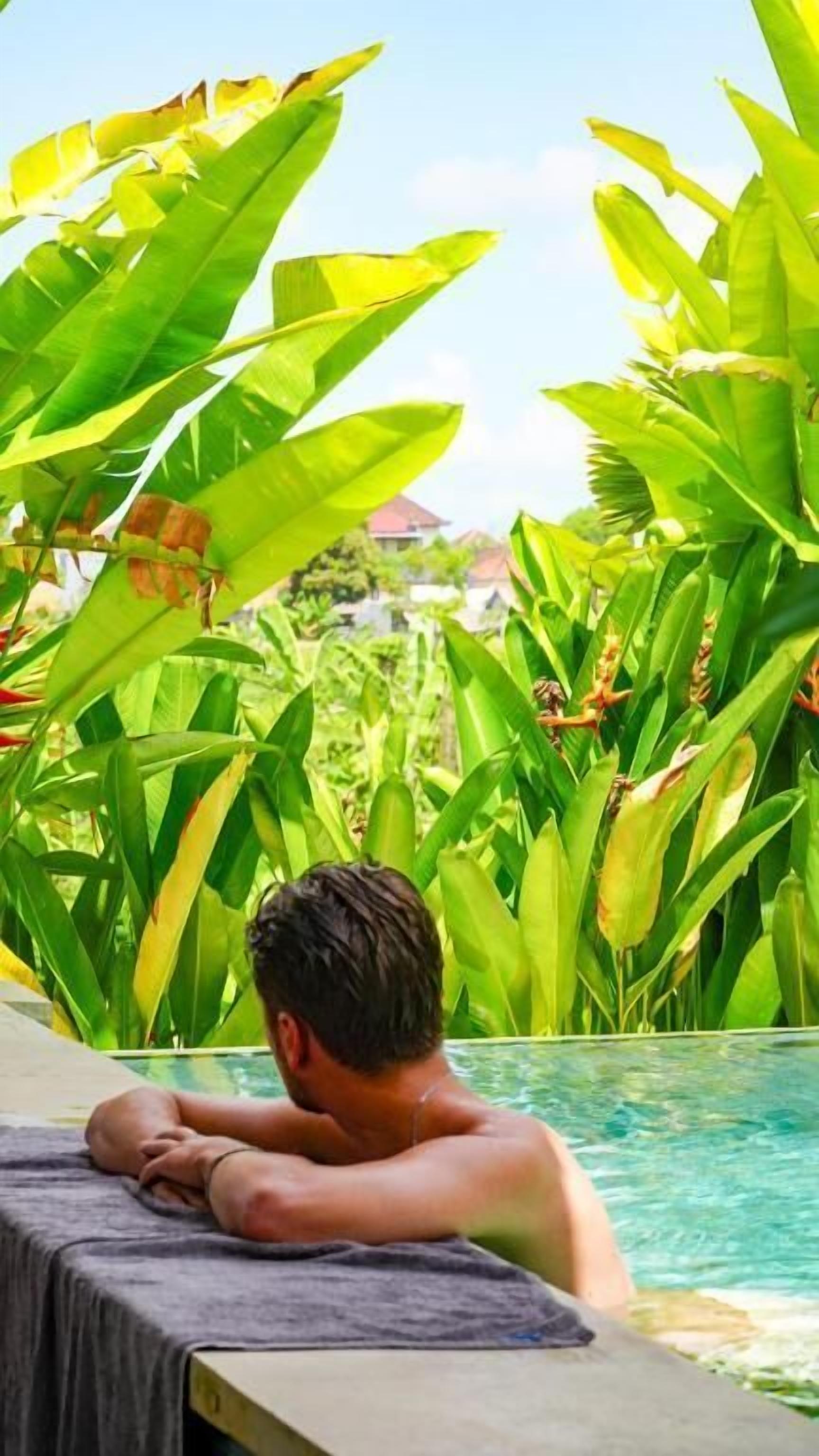 Una persona relaxant-se a la piscina, envoltada de vegetació exuberanta.