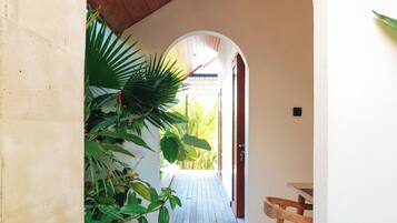 Um corredor com teto de madeira, chão de azulejos e vista para um jardim através de um arco aberto.