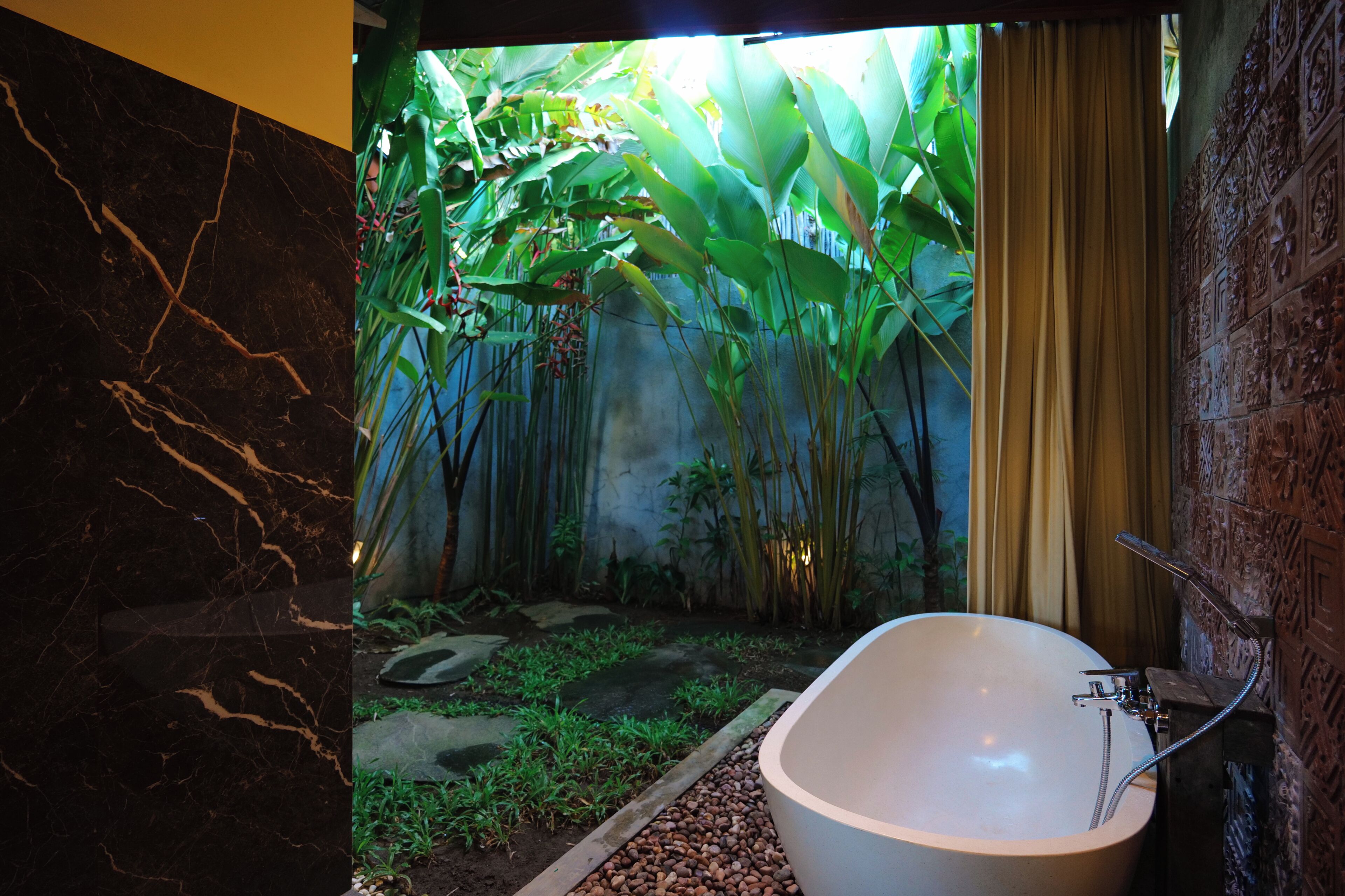 A bathroom with a bathtub, a shower, and a view of a tropical garden.