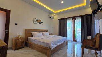 Quarto de hotel com cama de madeira, mesa de cabeceira, uma cadeira, televisão e uma janela grande com cortinas.