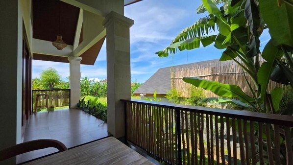 A wooden deck with a table and chairs, overlooking a garden with banana plants and a wooden fence.